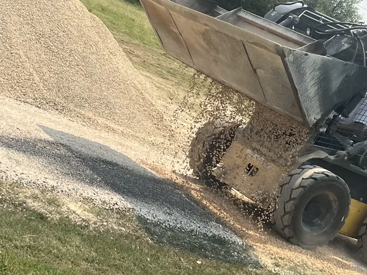 Skid steer spreading a load of crushed chip stone down a grassy slope
